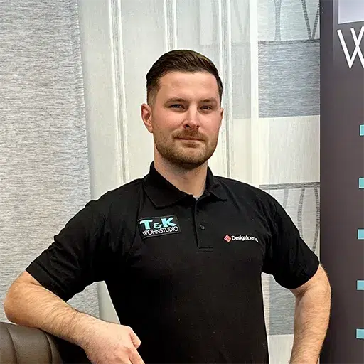 Ein Mann mit kurzen Haaren und Bart steht selbstbewusst da, eine Hand auf der Hüfte. In einem schwarzen Poloshirt von T&K Wohnstudio verkörpert er den „Über Uns“-Spirit und erscheint in einem Büro- oder Showroom-Ambiente, das Professionalität und Stil ausstrahlt. - Firmenadresse