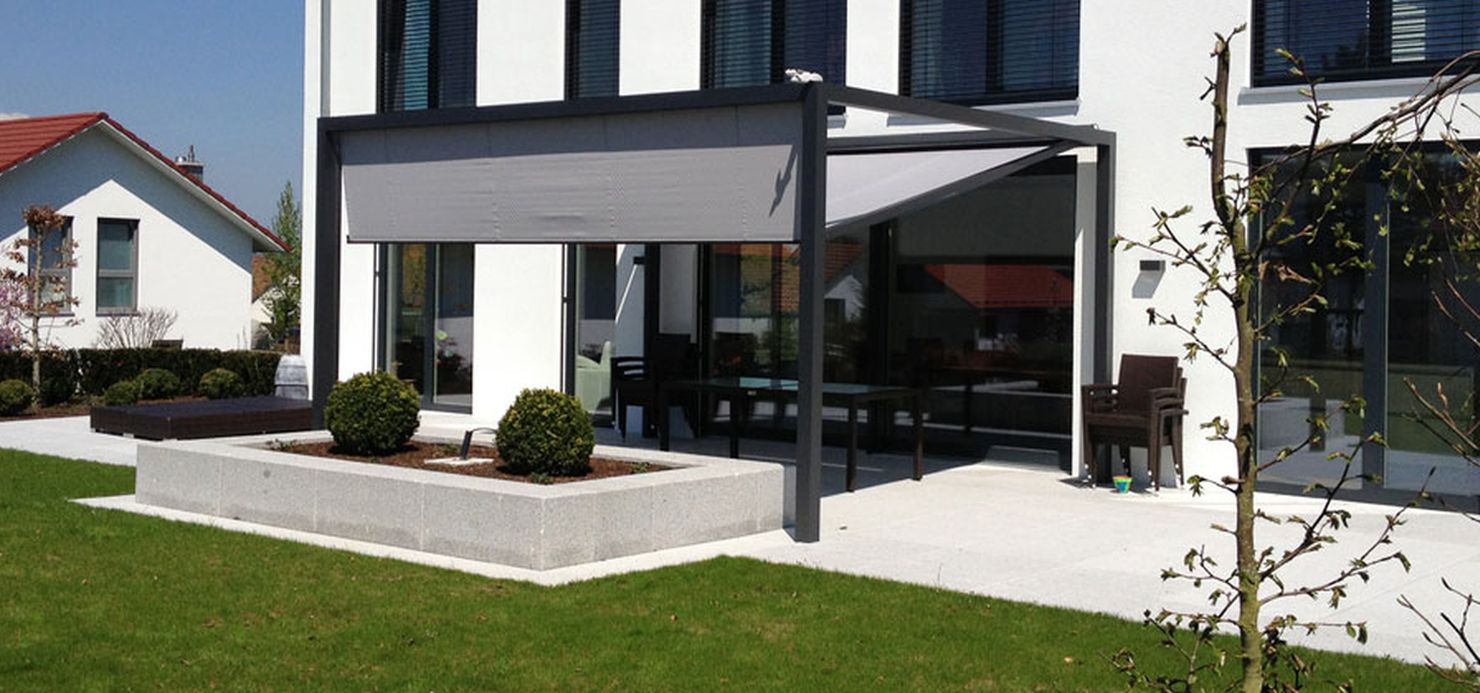 Modernes weißes Haus mit großen Fenstern, einem überdachten Terrassenbereich mit Markisen und Sitzgelegenheiten im Freien, Hochbeeten und einem gepflegten Rasen. - Farbenhaus Pflüger - Raumausstattung, Bodenbeläge, Vinylboden, Parkett, Farben, Malerarbeiten - Simmenet 2, 37235 Hessisch Lichtenau